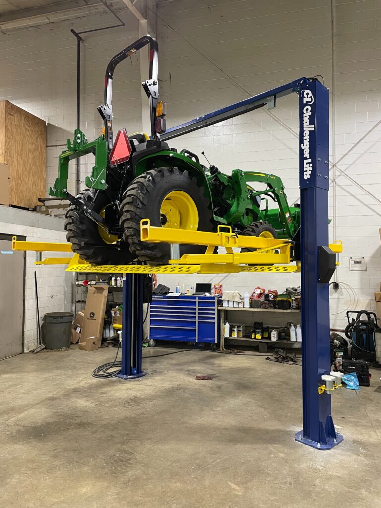 A two-post lift with a TurfRail adapter lifting a tractor