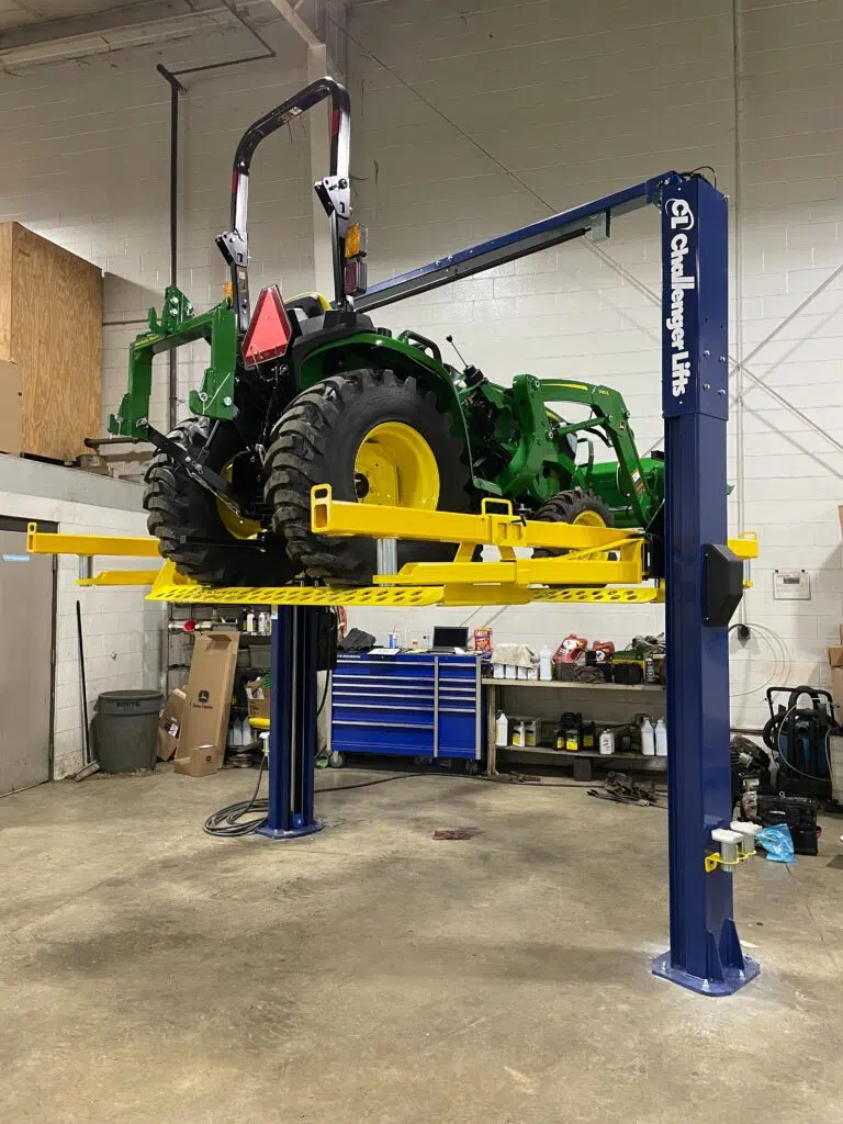 A two-post lift with a TurfRail adapter lifting a tractor